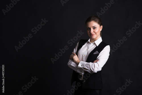 Portrait of a female business lady who crossed her arms in the studio on a black background with copyspace