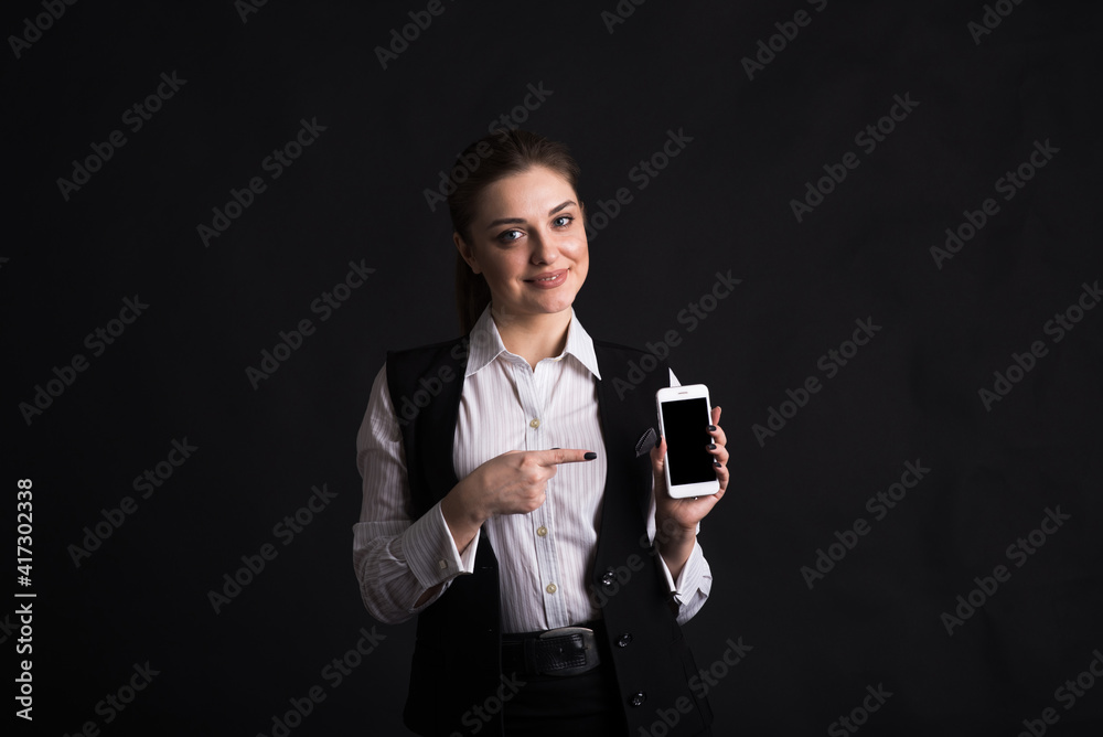 Portrait of a female business lady who points with a finger at the screen of her smartphone in the studio on a black background Portrait of a female business lady who points with a finger at the screen of her smartphone in the studio on a black background