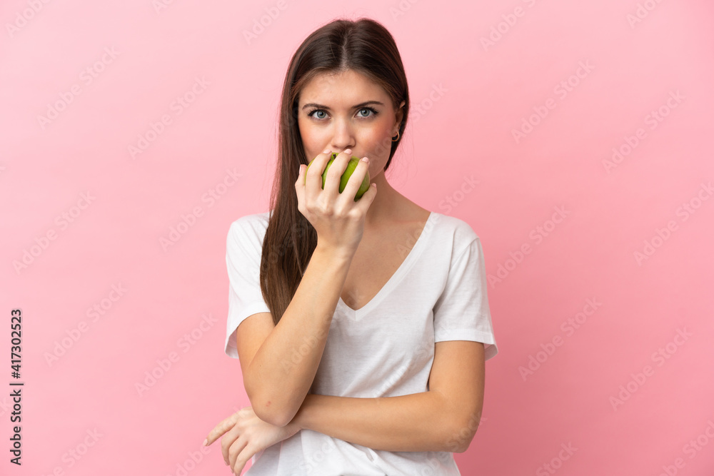 Young caucasian woman isolated on pink background eating an apple Young caucasian woman isolated on pink background eating an apple