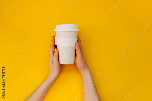 Female hands holding a reusable bamboo coffee cup on yellow background.