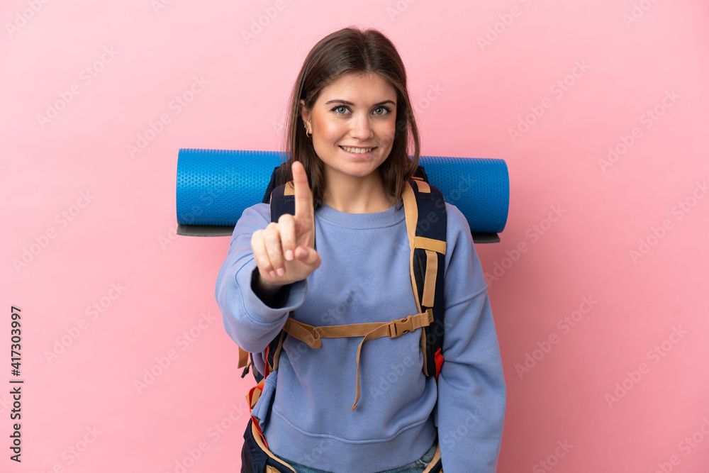 Young mountaineer woman with a big backpack isolated on pink background showing and lifting a finger Young mountaineer woman with a big backpack isolated on pink background showing and lifting a finger