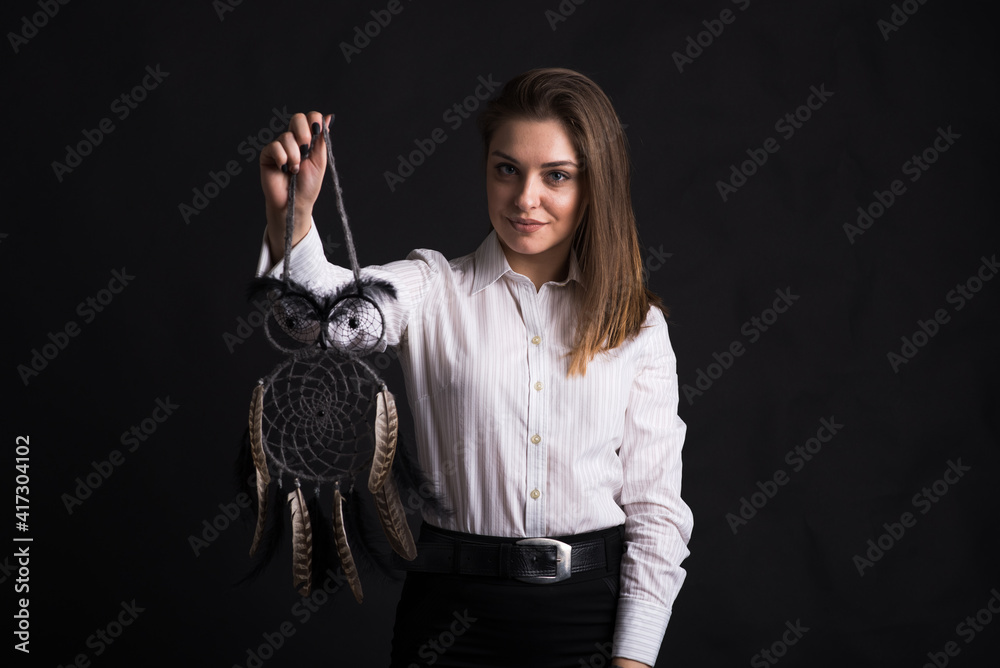 Young girl holding dreamcatcher in her arms in studio on black background