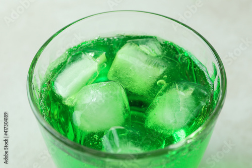 Glass of green soda on white textured background, close up
