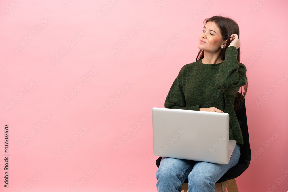 Young caucasian woman sitting on a chair with her laptop isolated on pink background having doubts and with confuse face expression Young caucasian woman sitting on a chair with her laptop isolated on pink background having doubts and with confuse face expression