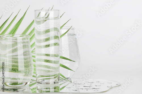 palm leaf distorted through water in glasses with mirror on white background. pure water , relax , surreal ,eco-friendly home concept. copy space. 