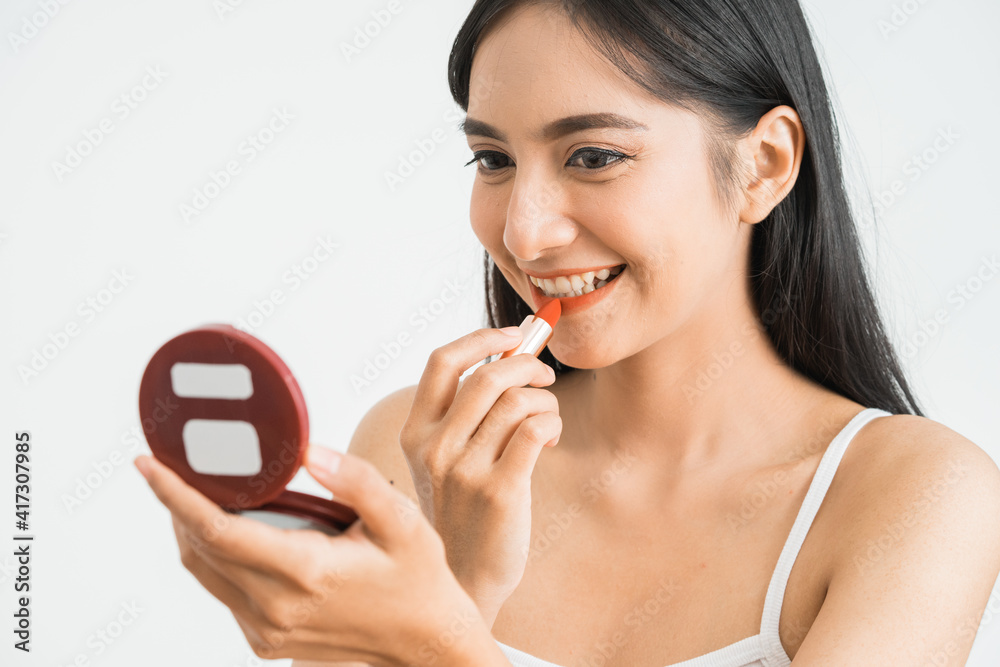 Lipstick makeup woman putting lip balm care. Beauty Asian girl applying cosmetic getting ready and looking at herself in the mirror smiling happy. Multi-ethnic Asian Caucasian model. Lipstick makeup woman putting lip balm care. Beauty Asian girl applying cosmetic getting ready and looking at herself in the mirror smiling happy. Multi-ethnic Asian Caucasian model.