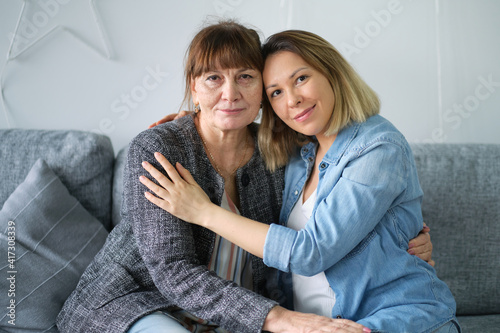 Head shot of beautiful adult daughter hug older mother at home, happy female two age generation family love
