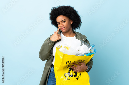 Young African American woman holding a recycle bag isolated on colorful background showing something