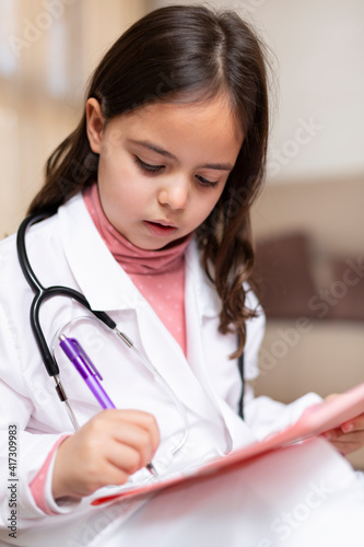 Close up of little girl dressed as a nurse handwriting a report. She is playing at being a doctor.