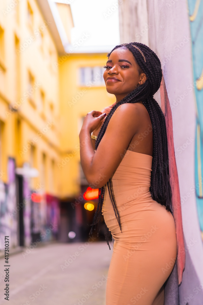 Trendy urban style with a black African girl in a cream colored dress on a city street. Posed back