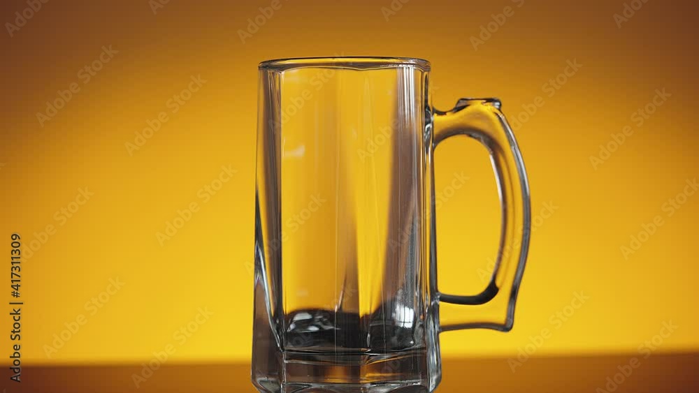 Slow motion shot of empty beer glass on orange background