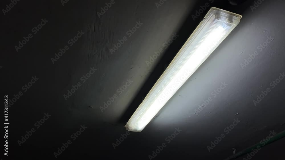 Broken flickering fluorescent lamp flashes on the ceiling of a dark room in underground parking lot