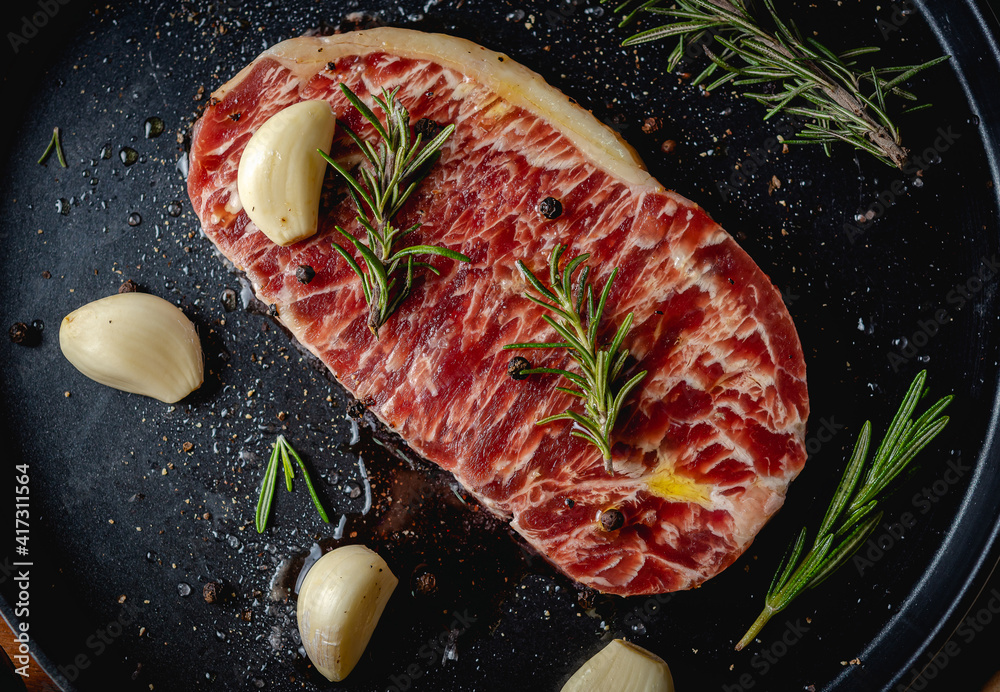 Raw fresh beef steak with olive oil, Colorful pepper, garlic and the rosemary leaf fresh on in the black tray on the wooden table, Top view.