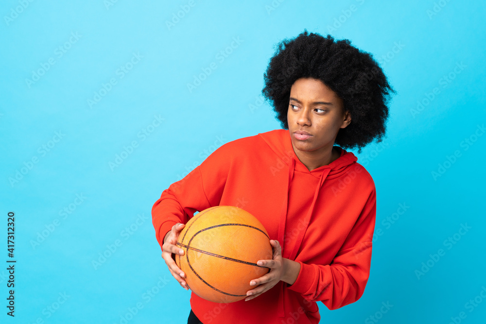 Young African American woman isolated on blue background playing basketball