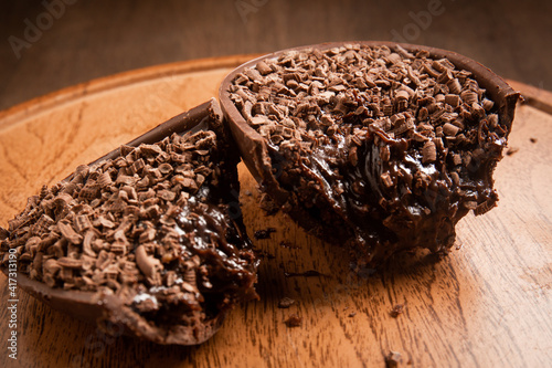 Canvas Print Cracked stuffed chocolate easter egg with grated chocolate on the top on a wooden stand on a wooden table