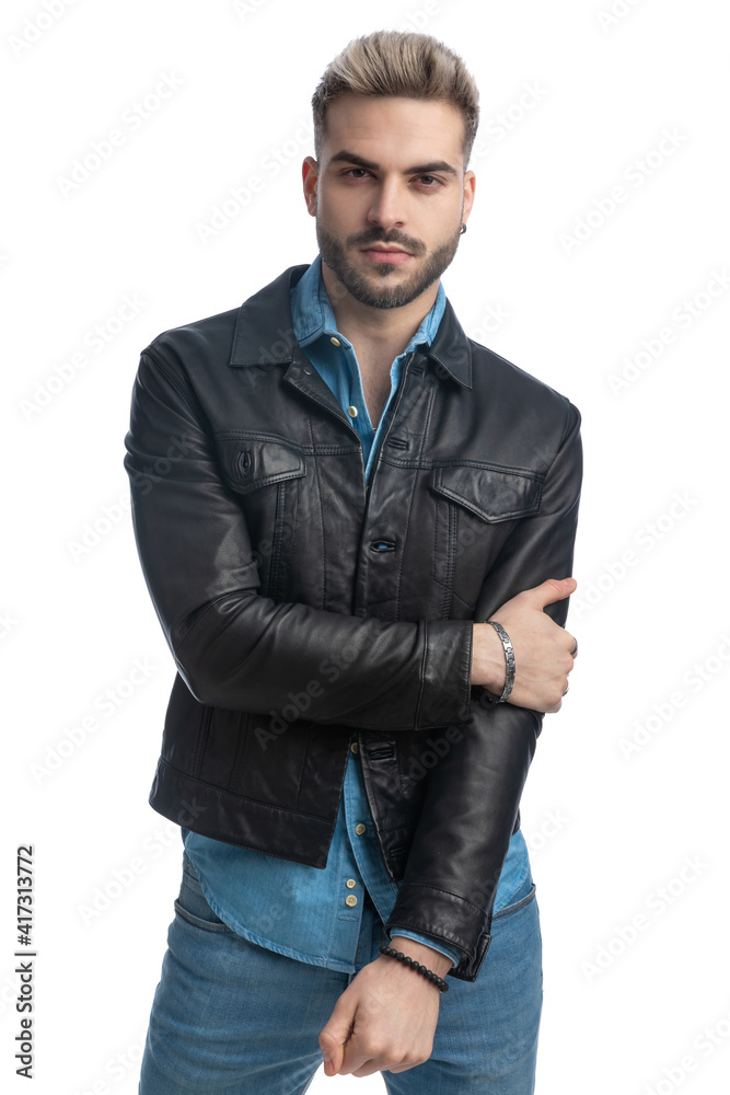 young casual biker guy in leather jacket holding arms in fashion pose young casual biker guy in leather jacket holding arms in fashion pose