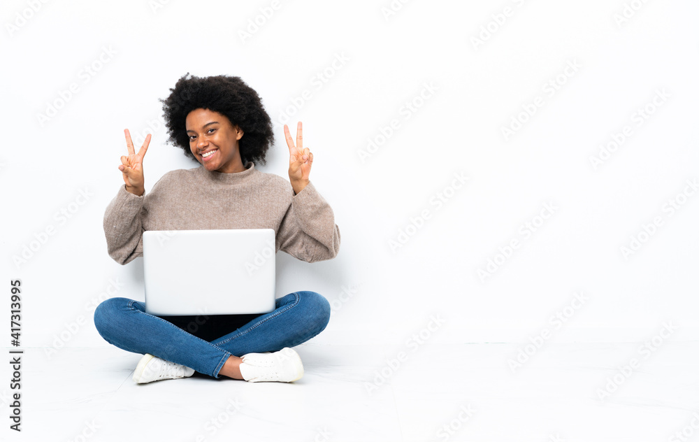 Young African American woman with a laptop sitting on the floor showing victory sign with both hands Young African American woman with a laptop sitting on the floor showing victory sign with both hands