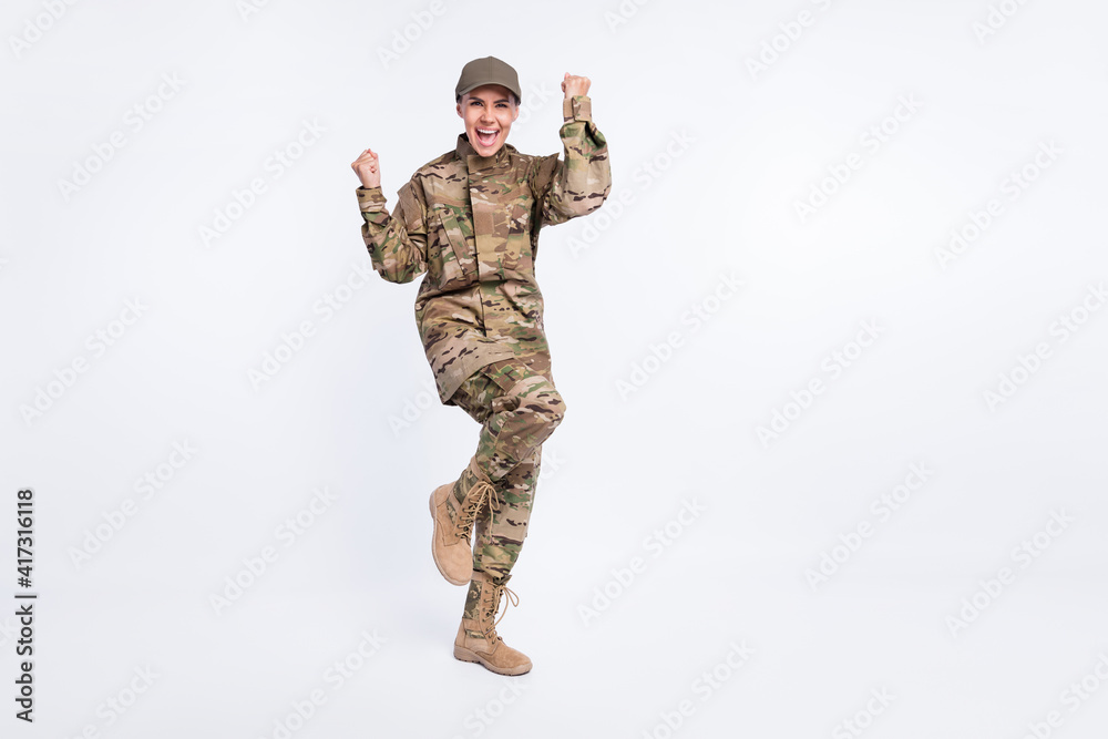 Full size photo of young woman soldier happy positive smile rejoice win victory fists hands isolated over white color background Full size photo of young woman soldier happy positive smile rejoice win victory fists hands isolated over white color background