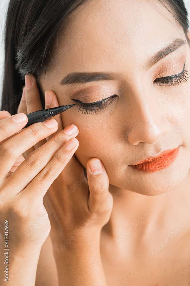 mixed race asian woman putting eye liner on eyelid on white background mixed race asian woman putting eye liner on eyelid on white background
