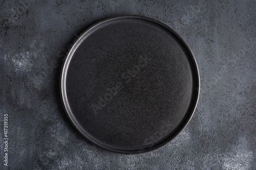 Empty round black plate on dark moody dark background with copy space. Overhead view