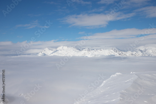 Snow peaks over clouds. Caucasus rocks. White mountains and blue sky.
