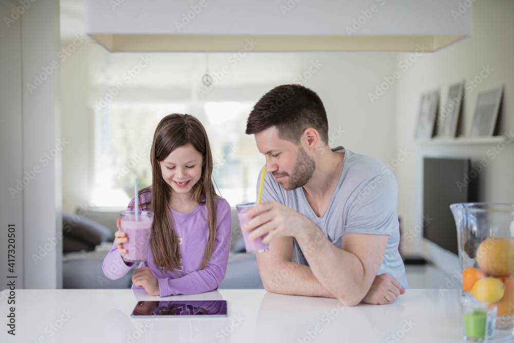 Father and daughter having smoothies while looking at digital table Father and daughter having smoothies while looking at digital table