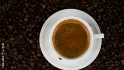 a pitchfork on top of a coffee pair a cup in a saucer, a cup of coffee with a gentle foam is poured, in the background blurred background everything is strewn with coffee beans
