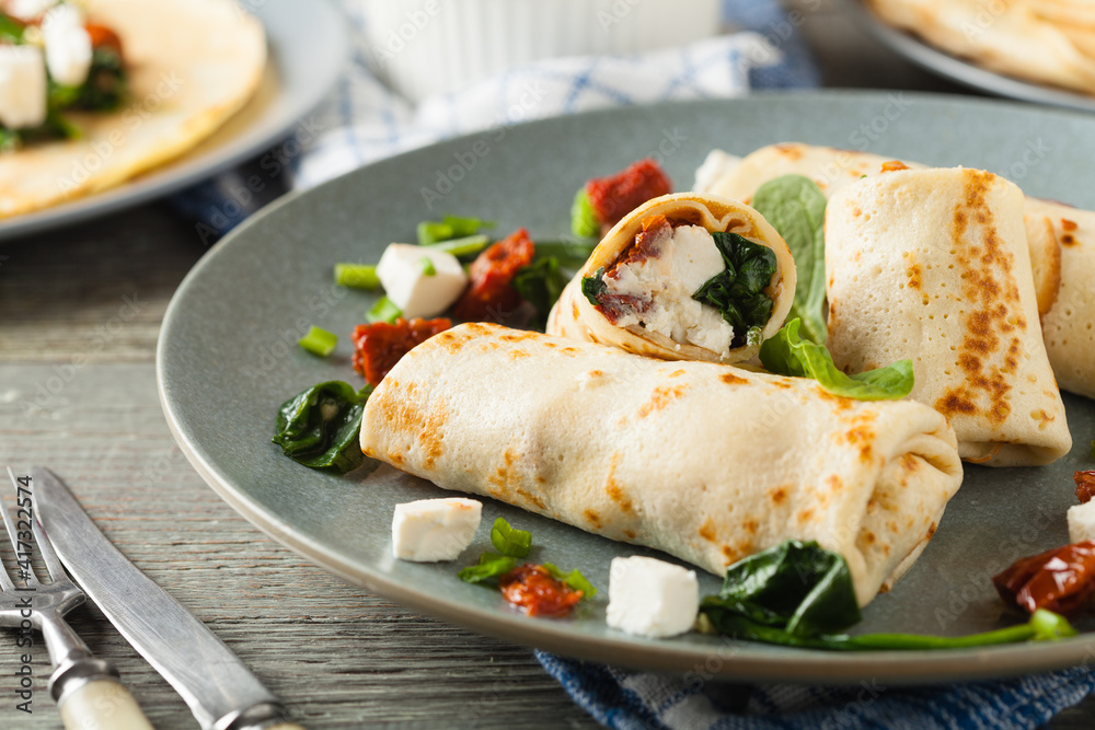 Pancakes with spinach, feta and dried tomatoes. Served on a gray plate. Wooden natural background. Pancakes with spinach, feta and dried tomatoes. Served on a gray plate. Wooden natural background.