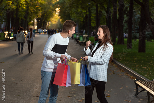 Young couple in love is funny considering shopping. Colored paper bags in hands