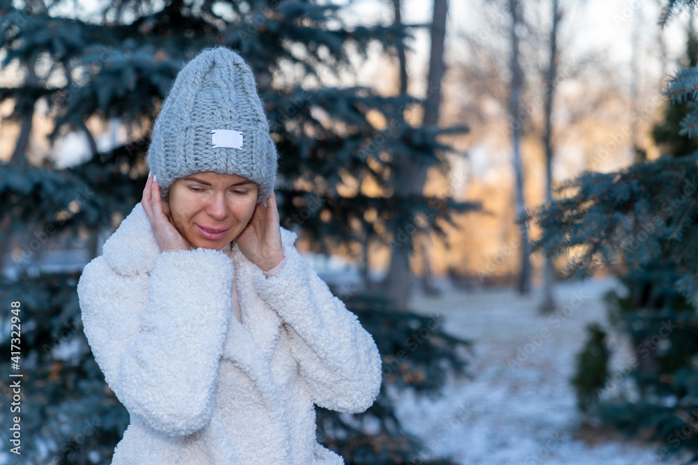 girl in a knitted woolen hat and a fur coat made of faux fur posing in a winter park standing against the background of fir trees girl in a knitted woolen hat and a fur coat made of faux fur posing in a winter park standing against the background of fir trees
