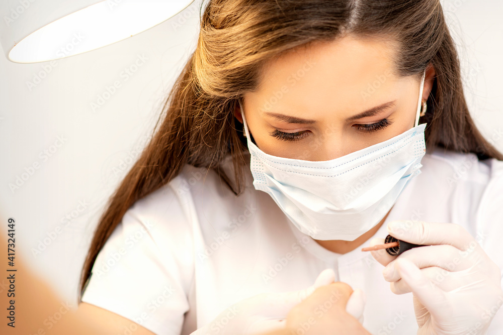 Manicure master in the white protective mask is painting nails with nail polish in a nail salon Manicure master in the white protective mask is painting nails with nail polish in a nail salon