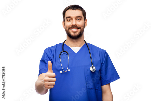 healthcare, profession and medicine concept - happy smiling doctor or male nurse in blue uniform with stethoscope showing thumbs up over white background