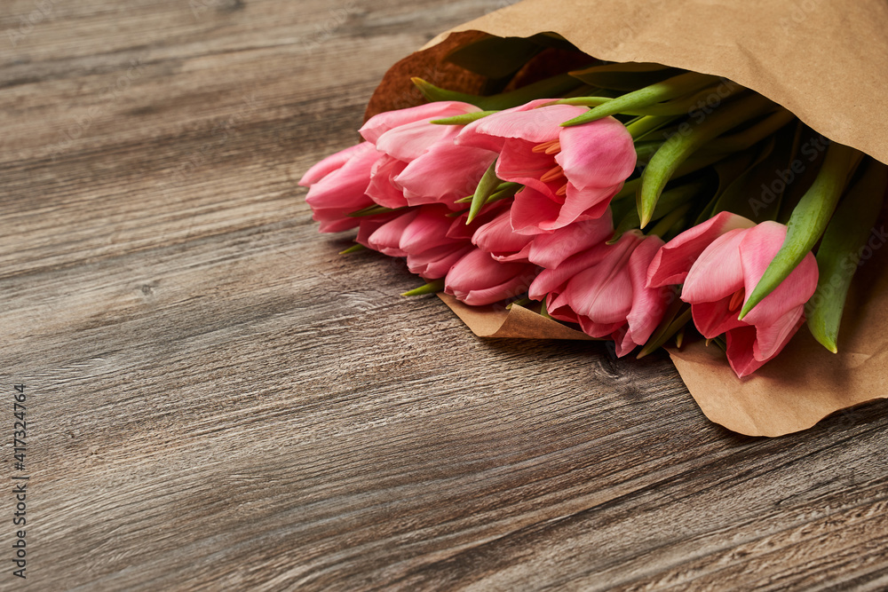 bouquet of pink tulips in craft paper on wooden background