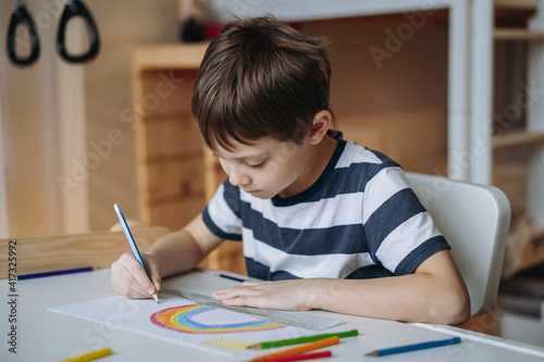 adorable caucasian boy of elementary age drawing with pencils sitting at the desk in his room at home. Image with selective focus