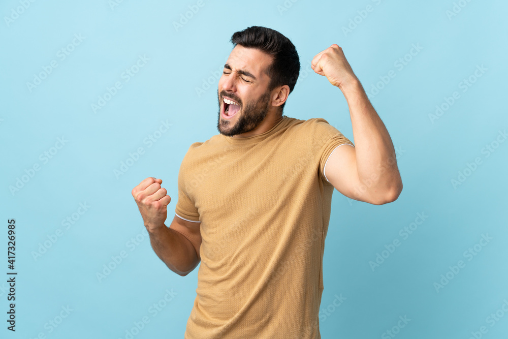 Young handsome man with beard over isolated background celebrating a victory Young handsome man with beard over isolated background celebrating a victory