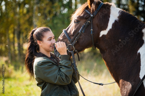 Cute girl talking with her horse after a joint walk in the background of the forest.