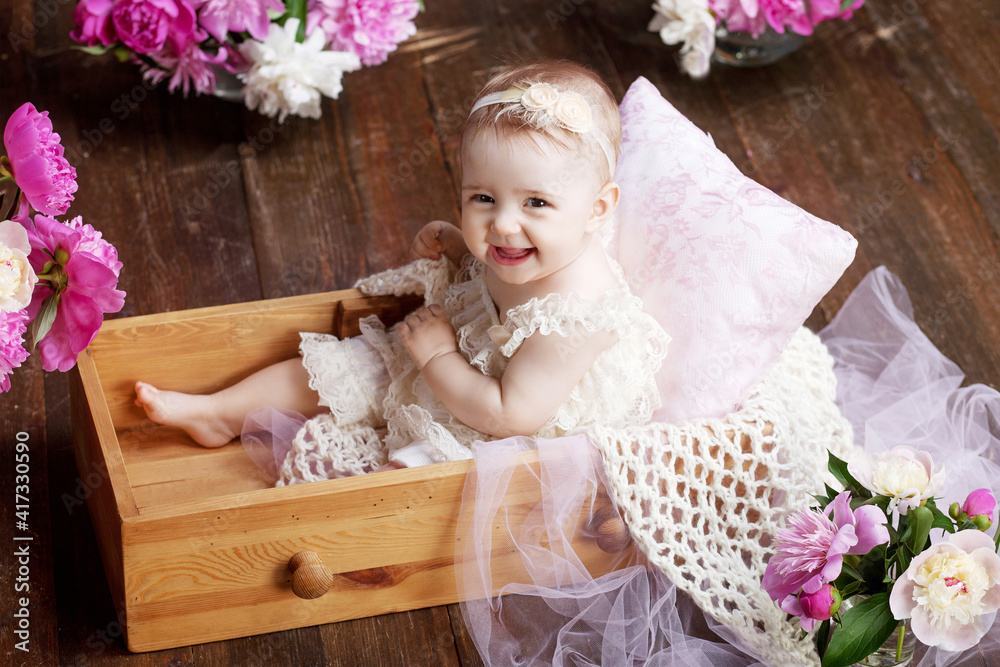 Portrait of a beautiful little baby girl with pink flowers. Sweet smiling girl sitting in wooden box on the floor Portrait of a beautiful little baby girl with pink flowers. Sweet smiling girl sitting in wooden box on the floor