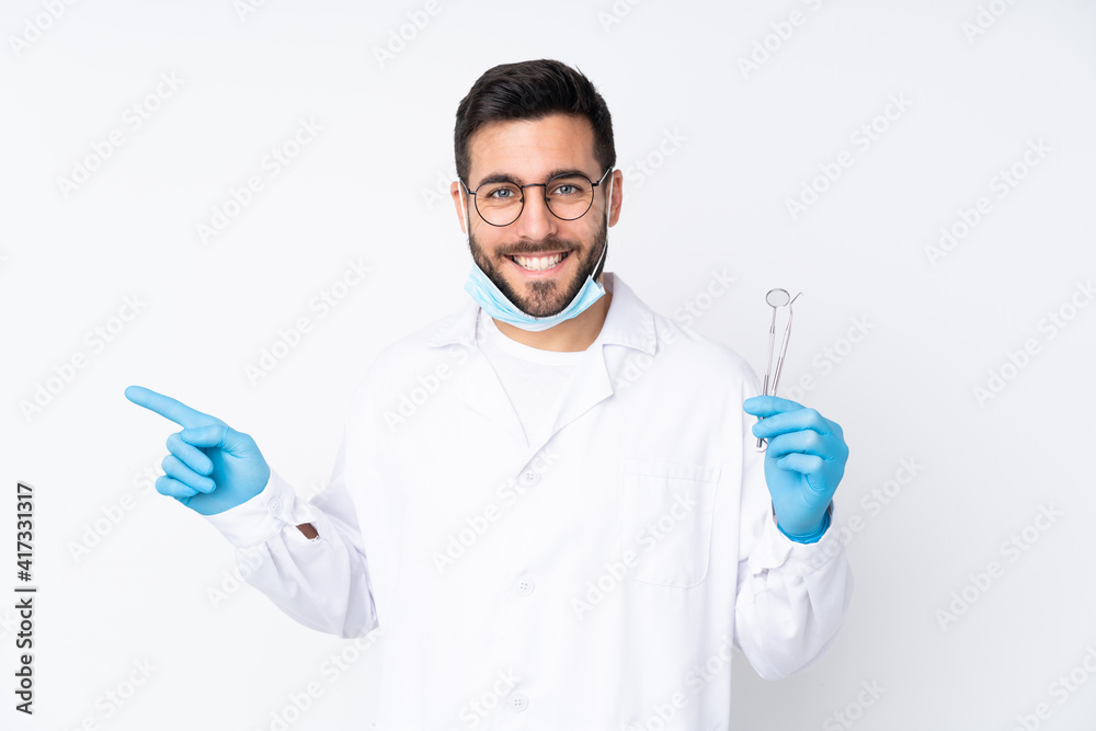 Dentist man holding tools isolated on white background pointing finger to the side Dentist man holding tools isolated on white background pointing finger to the side