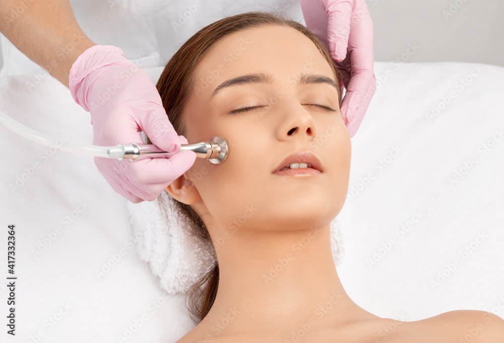 The cosmetologist makes the procedure Microdermabrasion of the face skin of a beautiful girl in a beauty salon.Cosmetology and professional skin care. The cosmetologist makes the procedure Microdermabrasion of the face skin of a beautiful girl in a beauty salon.Cosmetology and professional skin care.