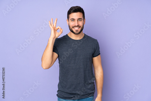 Caucasian handsome man showing ok sign with fingers over isolated purple background