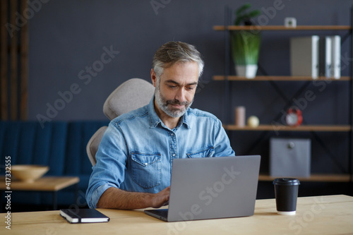Grey-haired senior man working in home office with laptop. Business portrait of handsome manager sitting at workplace. Studying online, online courses. Business concept.