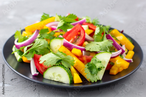 Plate of rainbow salad with different vegetables and herbs on black plate on grey stone background