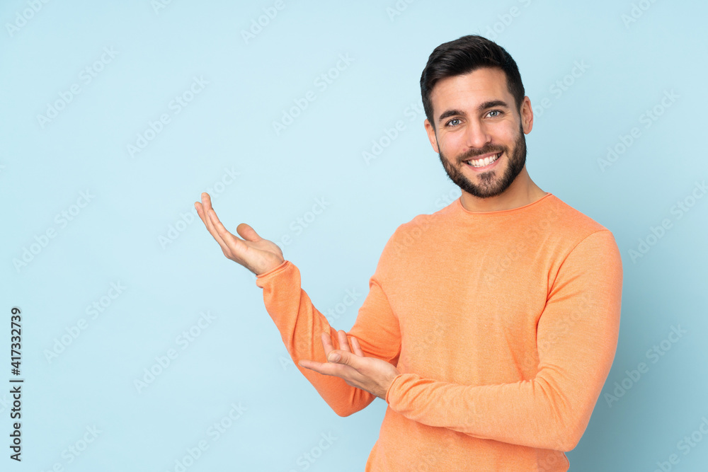 Caucasian handsome man extending hands to the side for inviting to come over isolated blue background Caucasian handsome man extending hands to the side for inviting to come over isolated blue background