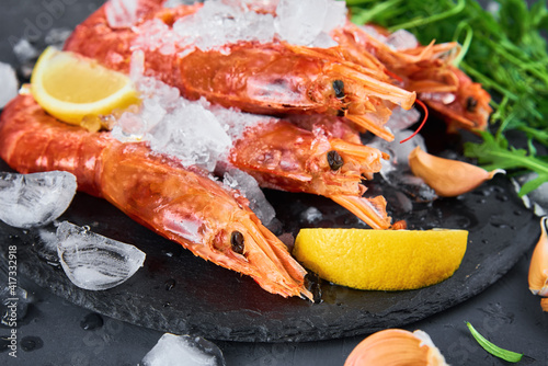 Frozen seafood. Fresh shrimps with lemon on dark background. Red raw prawns