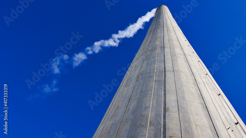 High smoke chimney in front of the blue sky. Central heating chimney. White smoke coming out of the chimney.