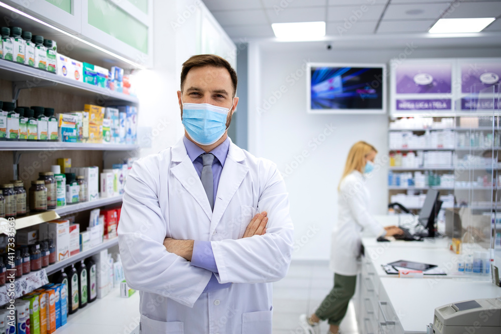 Portrait of handsome caucasian male pharmacist with face mask standing in pharmacy store.