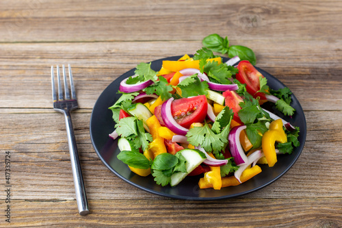 Plate of rainbow salad with different vegetables and herbs on black plate on wooden background