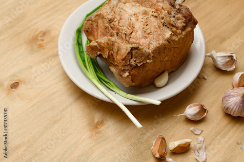 baked meat on a plate, green onion and garlic on wooden background, home cooking