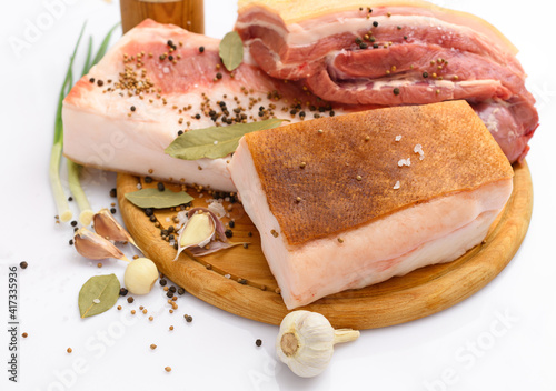 raw pork meat and lard with salt, spices and garlic on a cutting board, white background