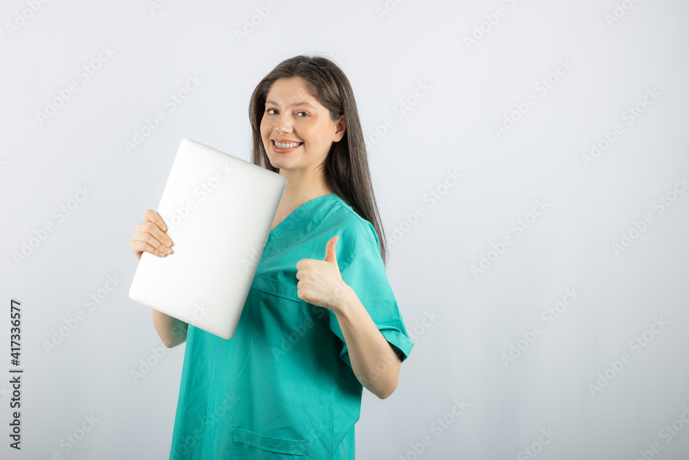 Photo of young nurse with laptop giving thumbs up on white background Photo of young nurse with laptop giving thumbs up on white background
